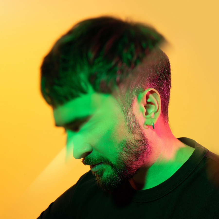 Artistic creative portrait through prism of a man looking down in green, pink neon lights on yellow background.