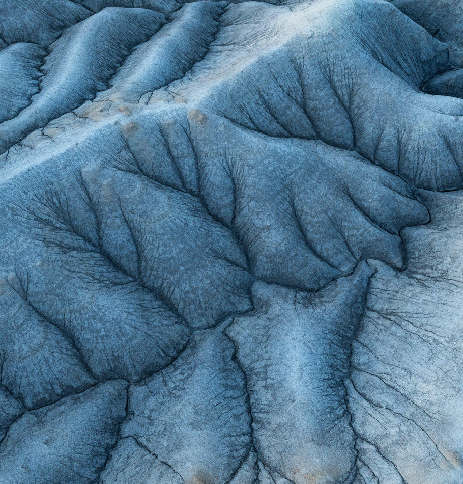 Overhead shot capturing the intricate textures and formations of blue-tinted badlands, highlighting their natural beauty and geological complexity